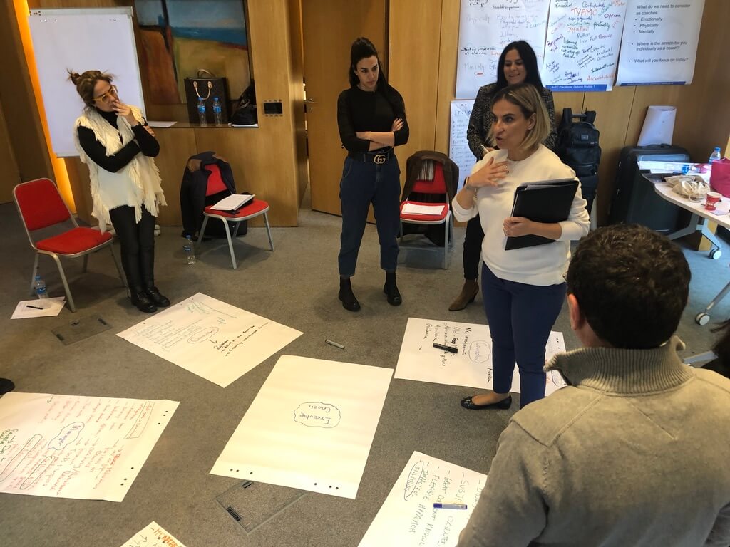 Leader giving direction to a team standing around workshop papers during a leadership session under authoritative leadership style.