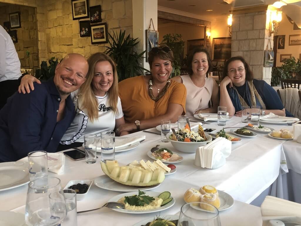 Five people smiling around a dining table showing connection in building a coaching culture.