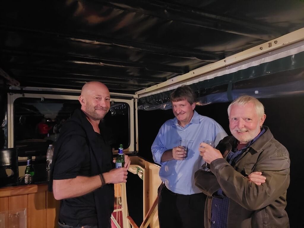 Three men standing on a boat at night, casually talking and holding drinks, showing trust and openness in a coaching culture at work.