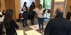 Leader giving direction to a team standing around workshop papers during a leadership session under authoritative leadership style.