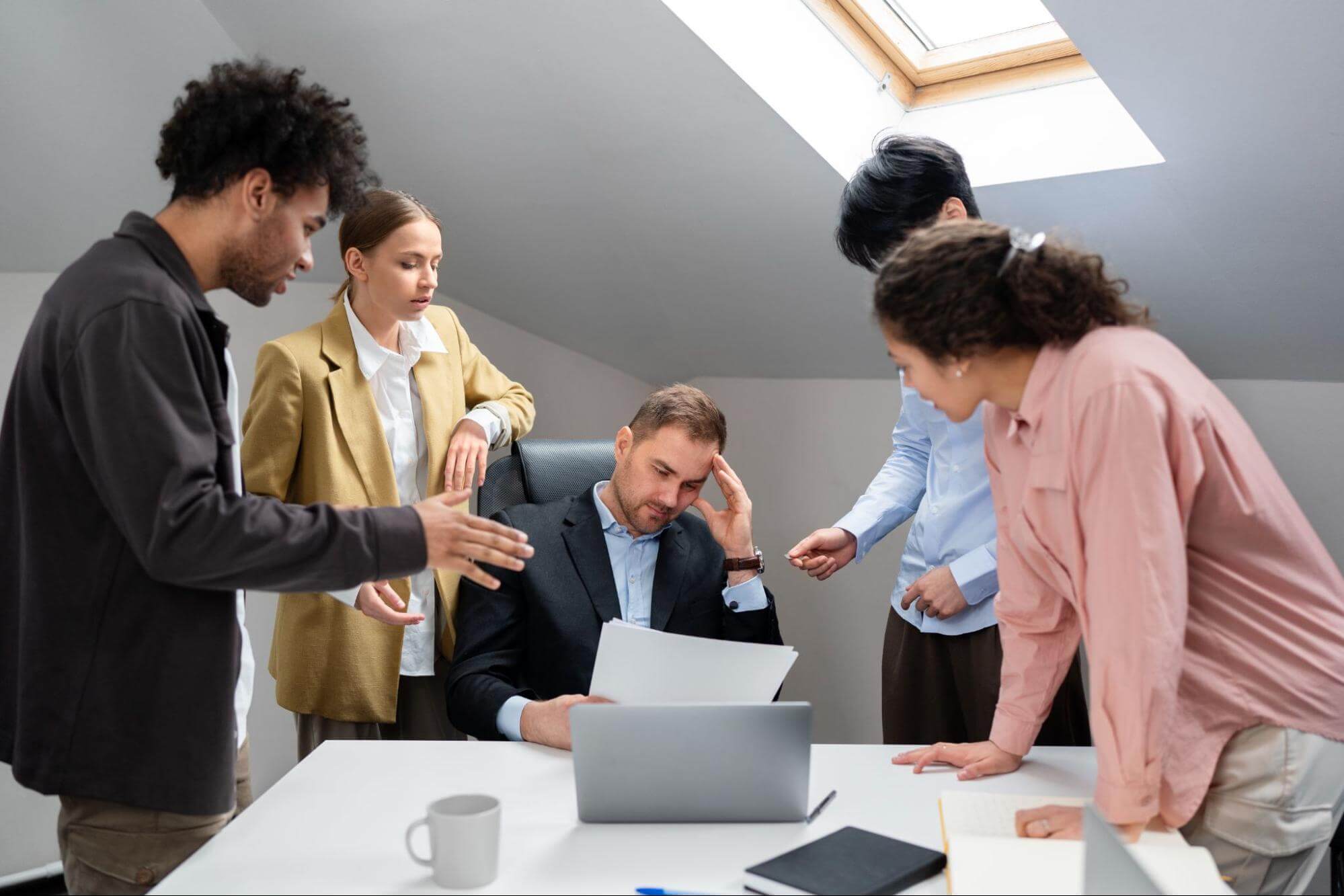 A group of office workers looking stressed around a desk, highlighting conflict resolution in a tense workplace discussion.