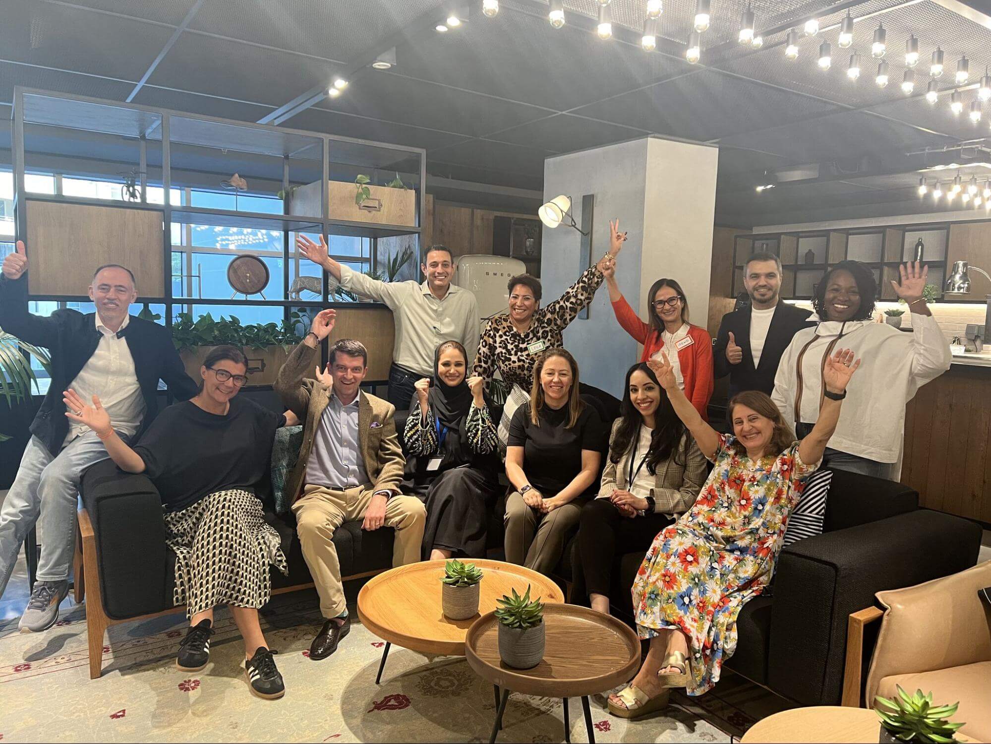 Coach Leila Rezaiguia celebrates with a large, diverse team in a modern office, showcasing effective people management.