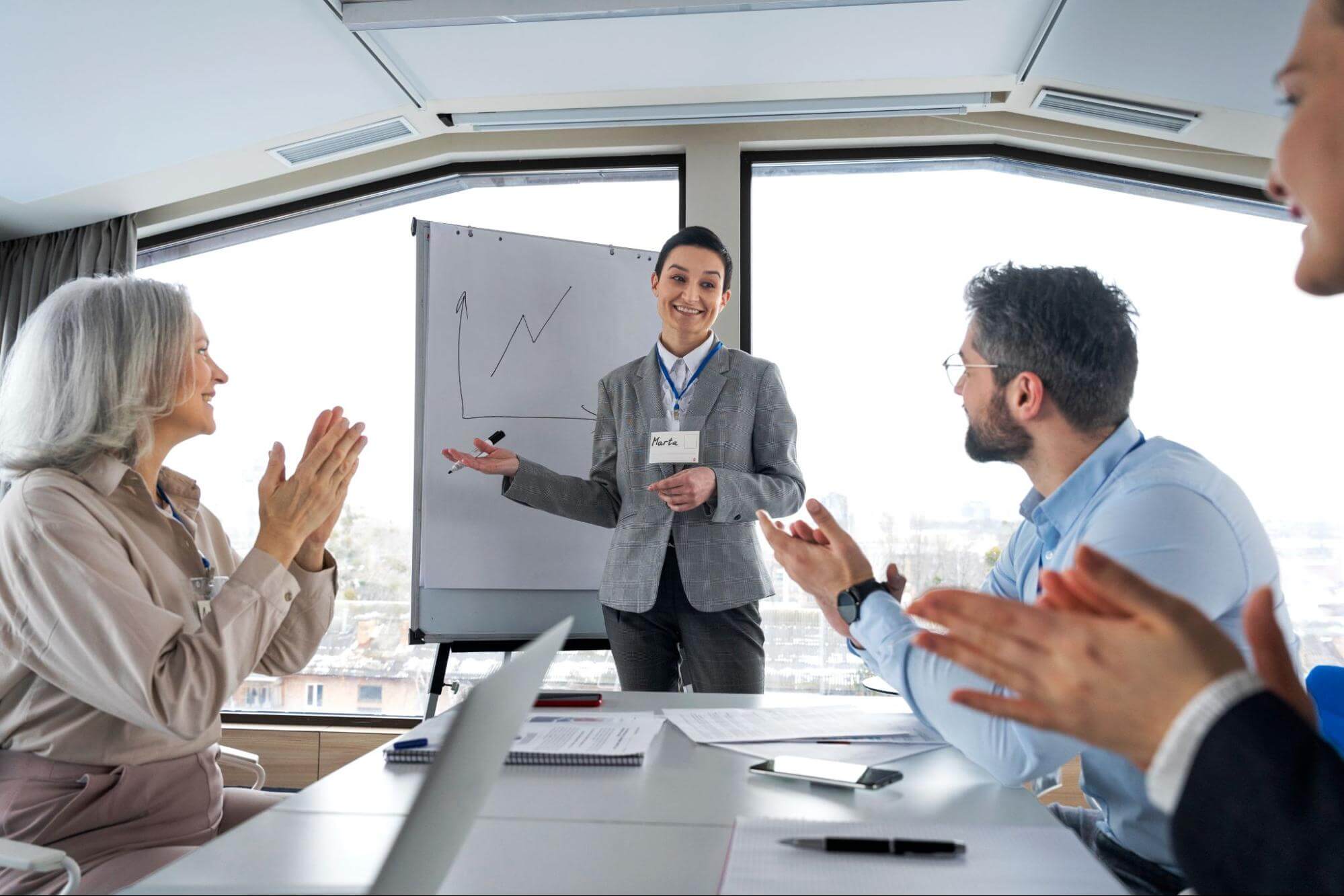 A presenter receives applause from colleagues during a business meeting, highlighting recognition of strong work ethic.
