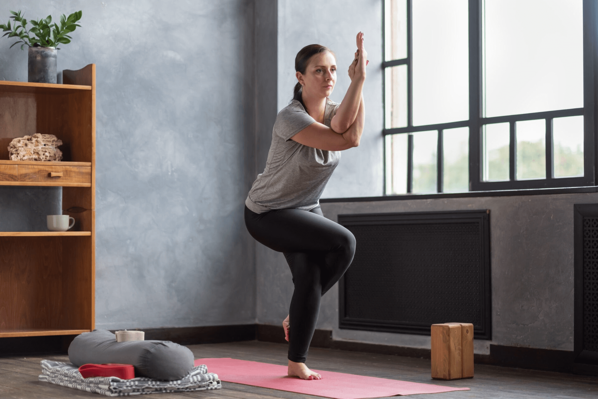 A woman performs Eagle Pose on a yoga mat.
