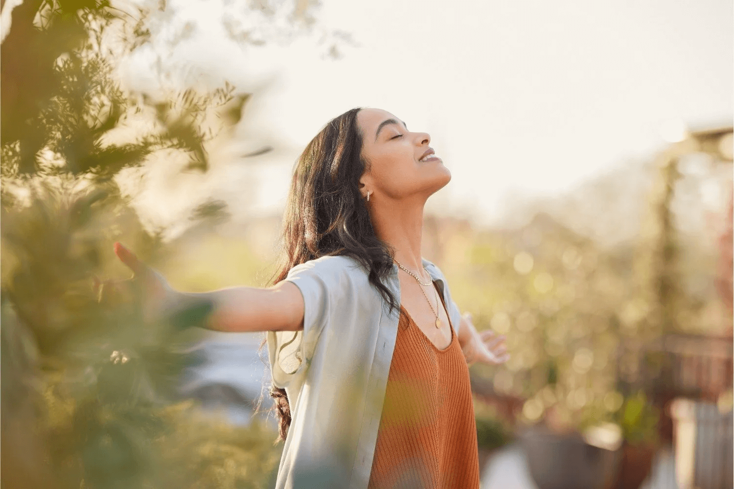 A woman stands outdoors with her arms outstretched, embracing the sunlight. 