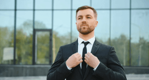 A suited man adjusts his jacket with a self-assured gaze, reflecting a sense of overconfidence.