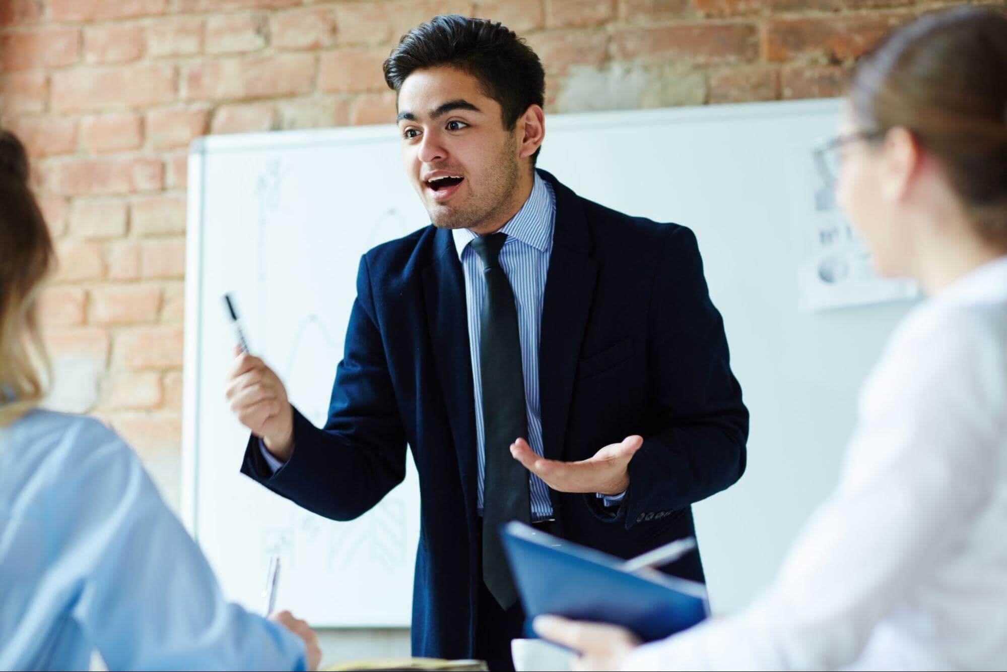 CEO mentor explaining ideas to a team, holding a pen and standing by a whiteboard.
