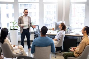 Mentor speaking to four professionals in a modern office with large windows.
