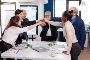 A diverse team stacking hands around a table, showing teamwork and interpersonal skills in a modern office.