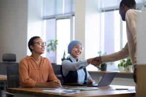 A woman in a hijab shakes hands with a man, showing ethics and integrity in the workplace.