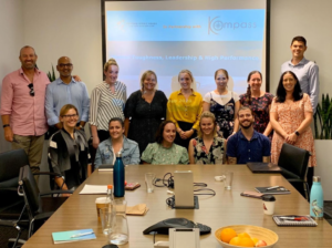 Young aspirants standing around a table, participating in a career development session with a projector screen behind them.